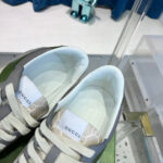 Sneakers Gucci moderne in verde oliva e grigio su superficie in vetro lucido.