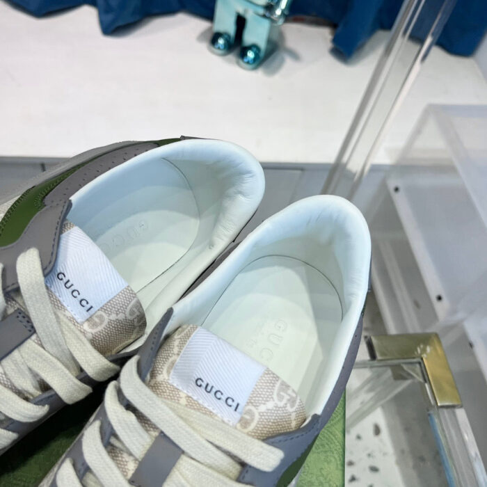 Sneakers Gucci moderne in verde oliva e grigio su superficie in vetro lucido.