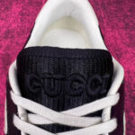Sneaker Gucci nera con dettagli beige e rosa su sfondo rosa testurizzato.