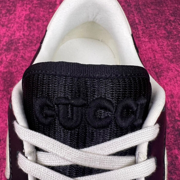 Sneaker Gucci nera con dettagli beige e rosa su sfondo rosa testurizzato.