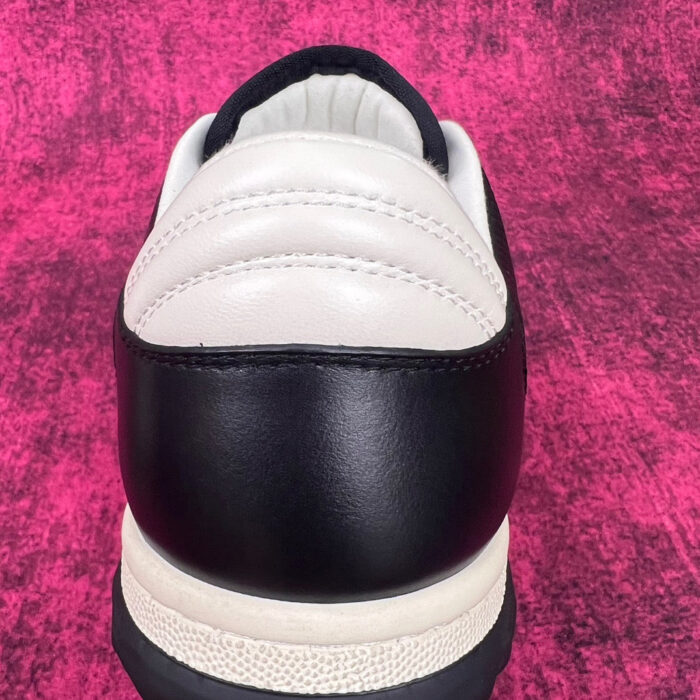Scarpa da sneaker bianco e nero su sfondo rosa vivace, stile moderno e sportivo.