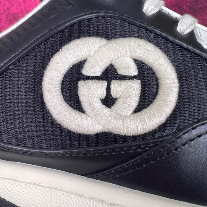Sneaker Gucci nera con logo ricamato su sfondo rosa, stile elegante e casual.