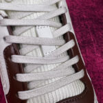 Sneaker moderna bianca e marrone con dettagli in tessuto, su sfondo colore profondo.