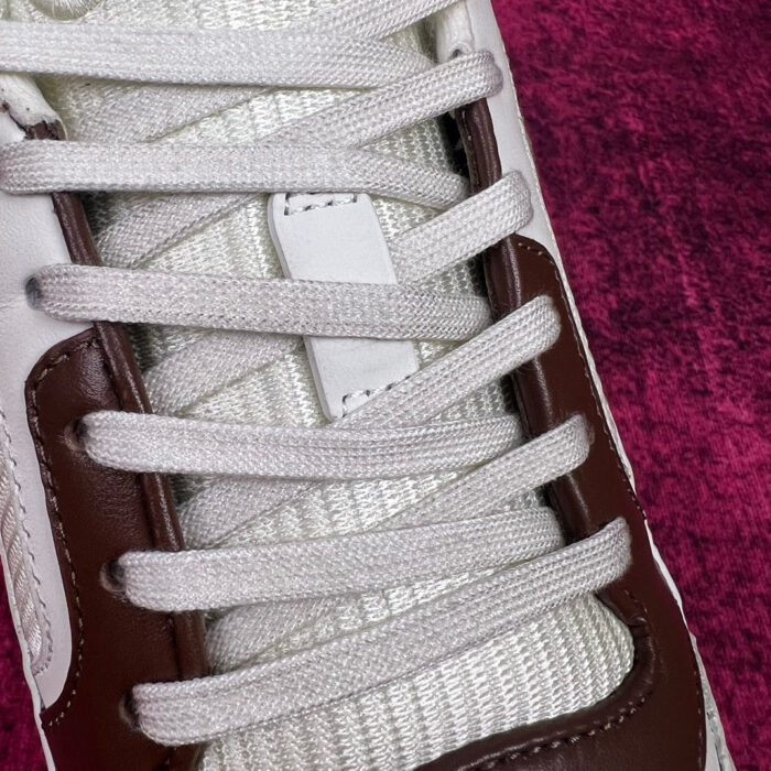 Sneaker moderna bianca e marrone con dettagli in tessuto, su sfondo colore profondo.