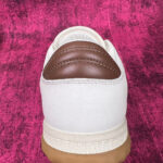 Sneaker bianca con dettaglio in pelle marrone su sfondo rosa, stile casual e moderno.