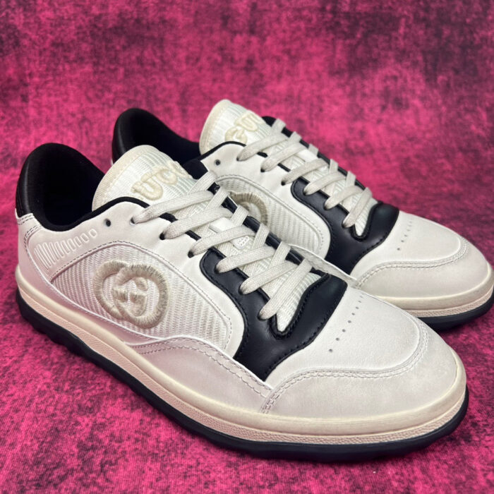Sneakers di lusso grigio e nero con logo embossato e tomaia in pelle, su sfondo rosa brillante.