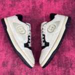 Sneakers bianche di lusso con logo circolare, su sfondo rosa vibrante.