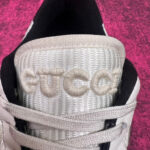 Sneaker Gucci bianca con logo ricamato e dettagli di lusso su sfondo fucsia vibrante.