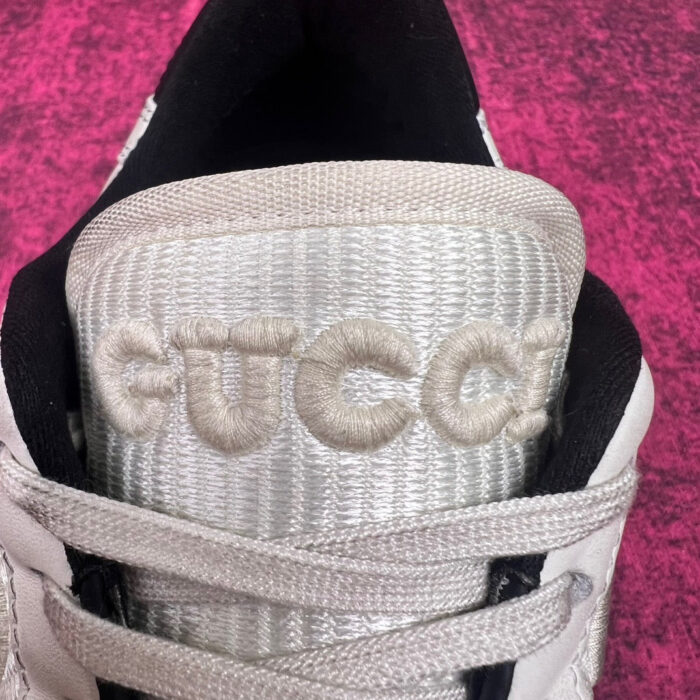 Sneaker Gucci bianca con logo ricamato e dettagli di lusso su sfondo fucsia vibrante.
