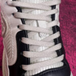 Sneaker moderna con lacci beige, dettagli neri e design elegante su sfondo rosa texture.