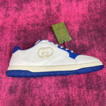Sneaker di lusso bianca e blu con logo in rilievo su sfondo rosa vibrante.