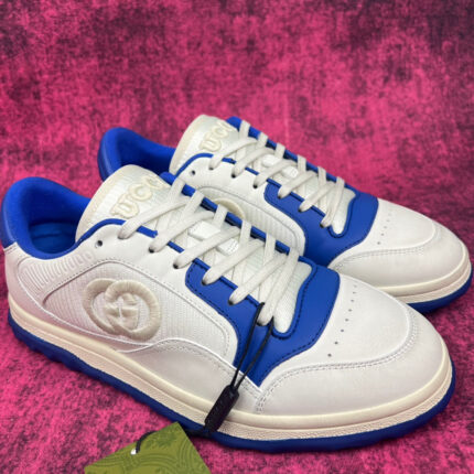 Sneakers bianche e blu moderne con logo embossato, stile sportivo e fashion su sfondo rosa vibrante.