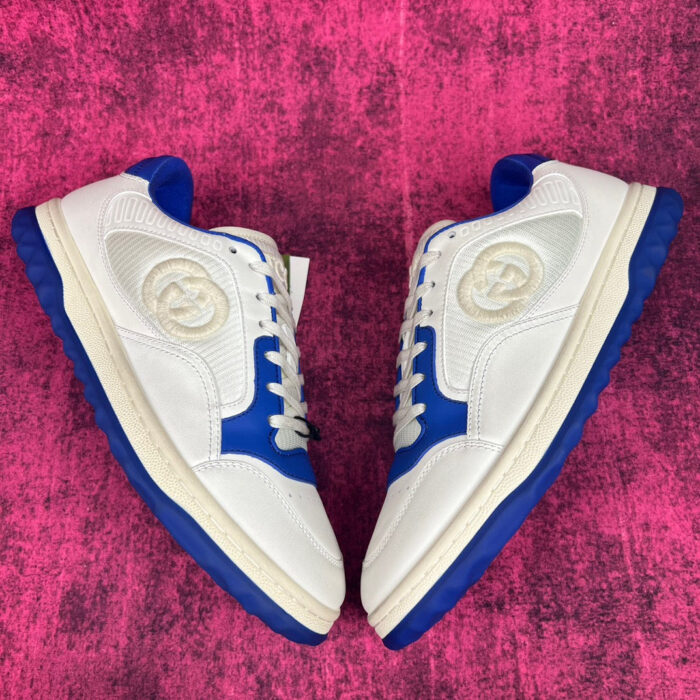 Sneakers bianche e blu con logo heritage su sfondo rosa vibrante.