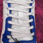 Sneaker bianca sportiva con dettagli blu, tessuto traspirante e design moderno.