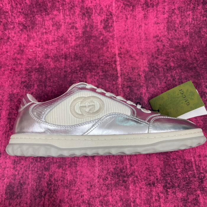 Sneaker Gucci bianca con dettagli iridescenti su sfondo rosa vibrante.