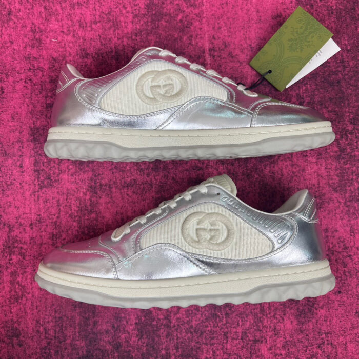 Sneakers silver metallizzate con logo lussuoso, suola resistente e stile moderno in backdrop rosa vibrante.