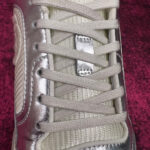 Sneaker moderna con lacci grigi, finish metallici e design elegante su sfondo borgogna.