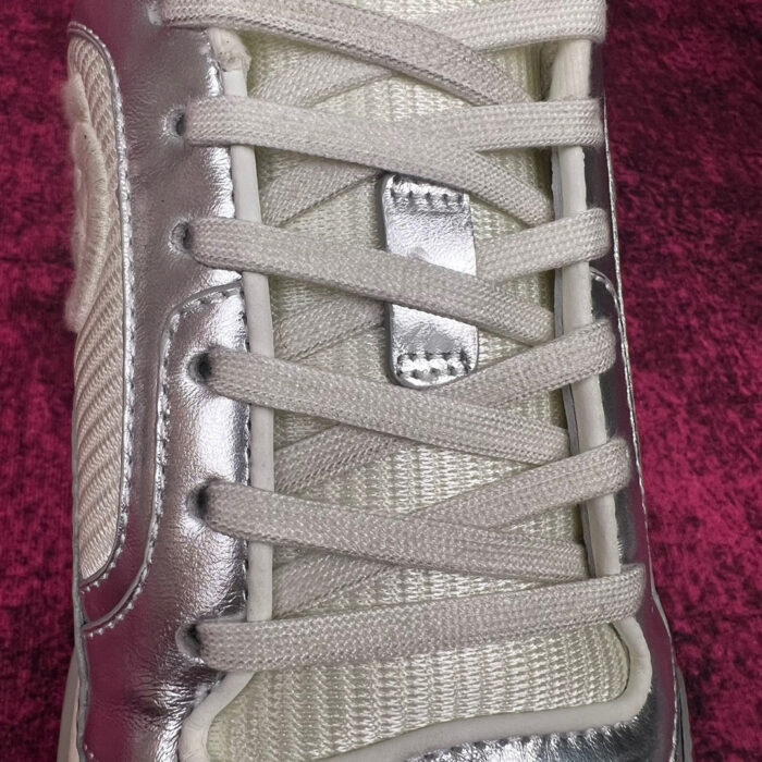 Sneaker moderna con lacci grigi, finish metallici e design elegante su sfondo borgogna.