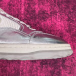 Sneaker silver moderna con dettagli di contrasto su sfondo rosa vibrante.