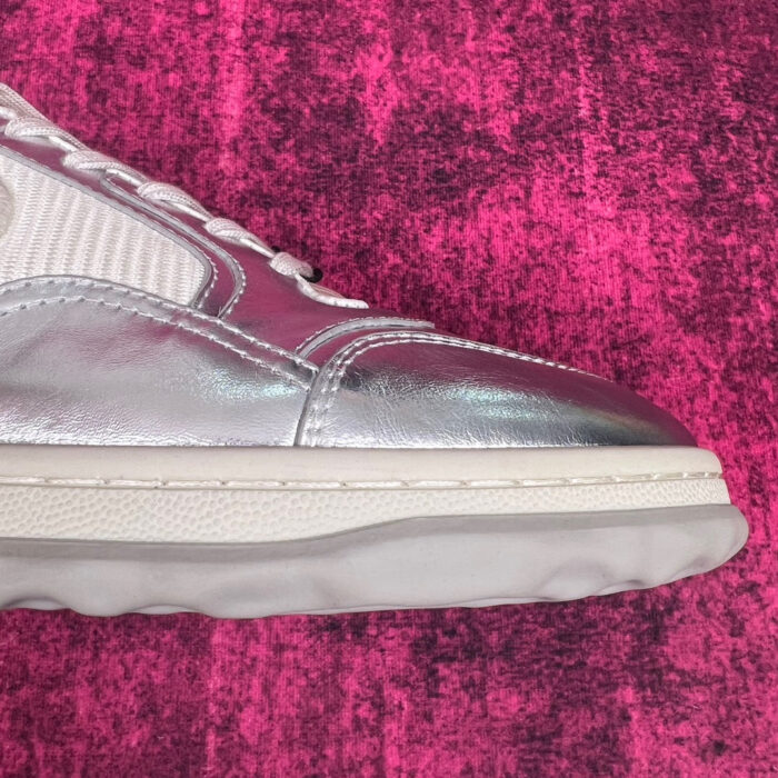 Sneaker silver moderna con dettagli di contrasto su sfondo rosa vibrante.
