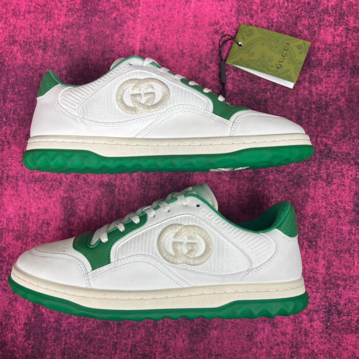 Sneakers luxury Gucci con dettagli verdi e logo, su sfondo rosa vivace.