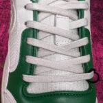 Sneaker bianca e verde con dettagli moderni, lacci robusti e materiali di alta qualità.