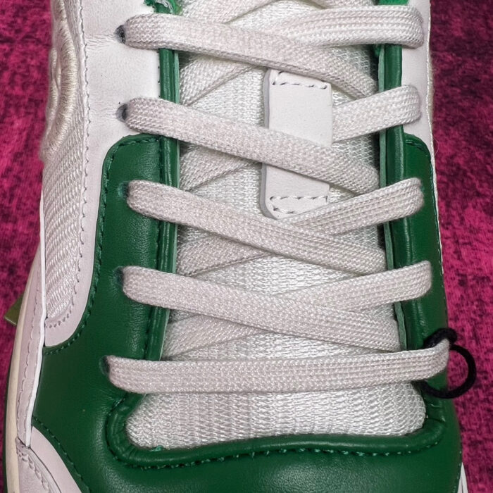 Sneaker bianca e verde con dettagli moderni, lacci robusti e materiali di alta qualità.