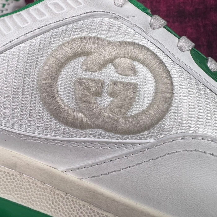 Sneaker bianca di lusso con logo ricamato e dettagli verdi, stile moderno ed elegante.