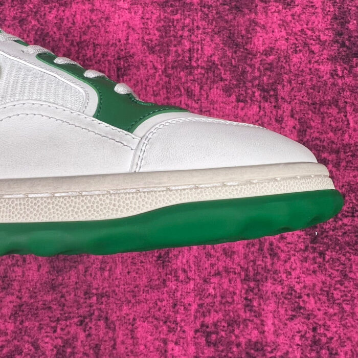 Sneaker bianca con dettagli verdi su sfondo rosa vivace, stile sportivo e moderno.