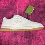 Sneaker Gucci bianca con suola trasparente, dettagli verdi e design elegante su sfondo rosa.