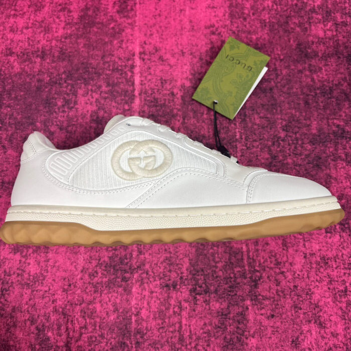 Sneaker Gucci bianca con suola trasparente, dettagli verdi e design elegante su sfondo rosa.