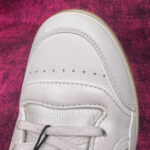 Sneaker raffinata in pelle grigia con dettagli perforati e design minimalista su sfondo colorato.