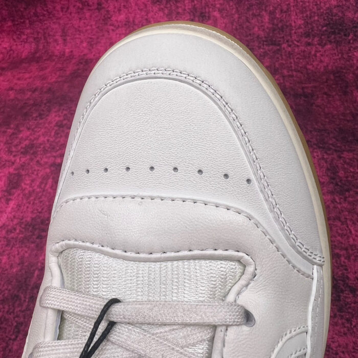 Sneaker raffinata in pelle grigia con dettagli perforati e design minimalista su sfondo colorato.