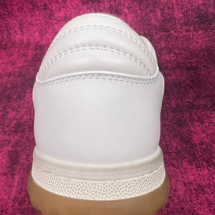 Sneaker bianca con suola in gomma su sfondo rosa vibrante, stile minimalista e moderno.