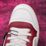 Sneaker bianca con dettagli rossi su sfondo rosa vibrante, stile moderno e design accattivante.