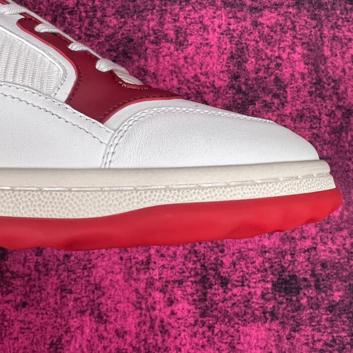 Sneaker bianca moderna con dettagli rossi, su sfondo rosa: stile streetwear e comfort.