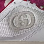 Sneaker Gucci bianca con logo interlock, dettagli rossi e sfondo rosa elegante.