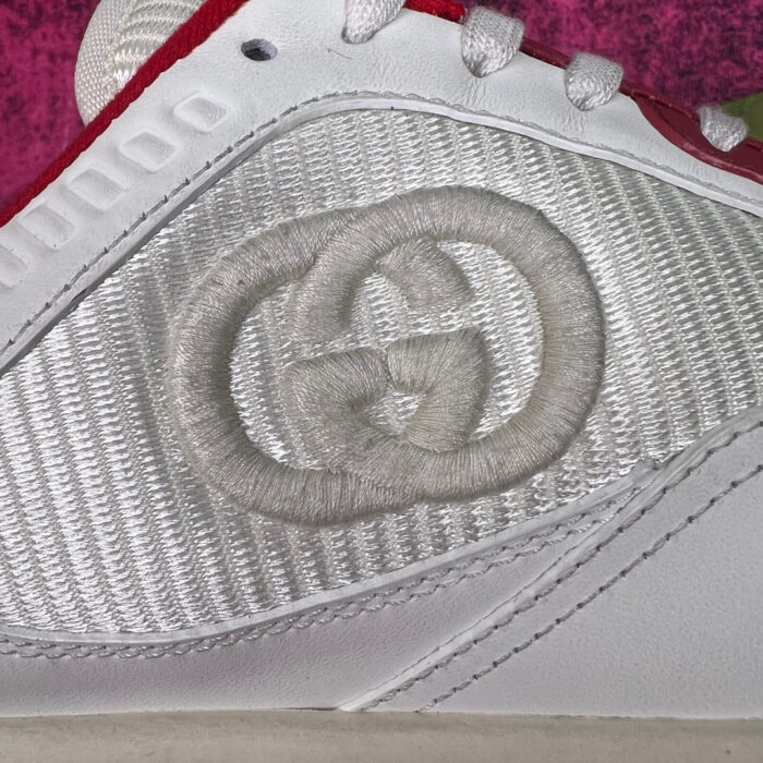 Sneaker Gucci bianca con logo interlock, dettagli rossi e sfondo rosa elegante.