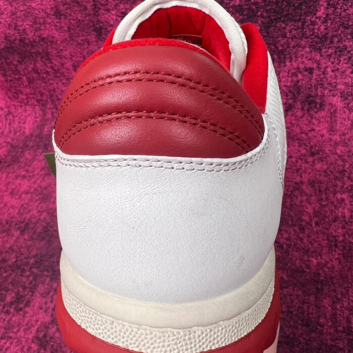 Sneaker bianca con dettagli rossi, design moderno e comfort, su sfondo viola vibrante.
