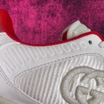 Sneaker moderna bianca con dettagli ricamati e accenti rossi, su sfondo viola textured.