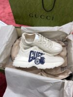 Sneakers Gucci beige di lusso su sfondo rosso, stile casual e trendy.