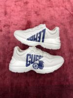 Sneakers Gucci moderne in bianco, con dettagli Navy su sfondo rosso cremisi elegante.