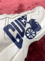 Sneaker Gucci bianca con logo blu e dettagli bike, stile moderno e confortevole.
