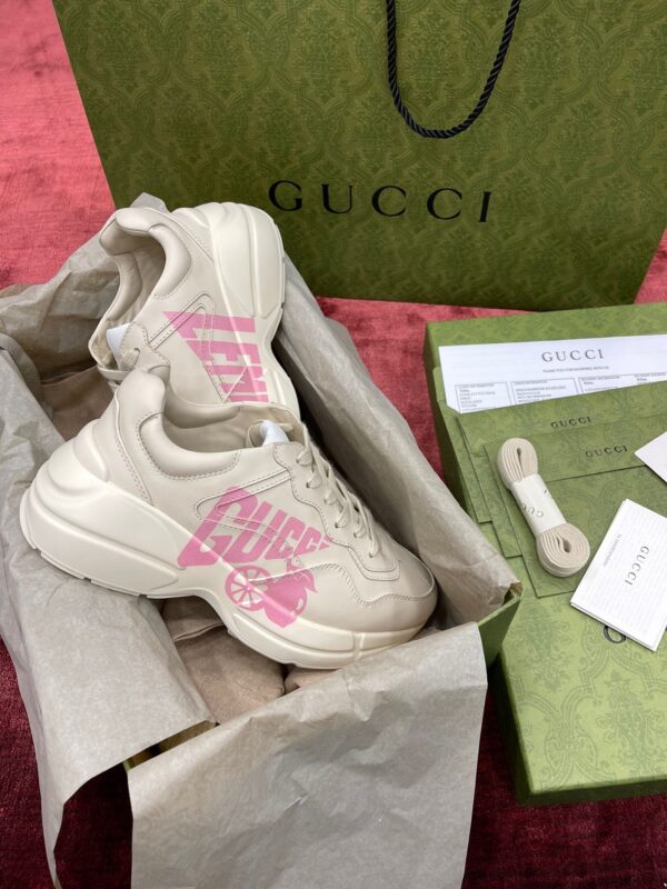Sneakers beige Gucci con dettaglio rosa, packaging di lusso e design contemporaneo elegante.