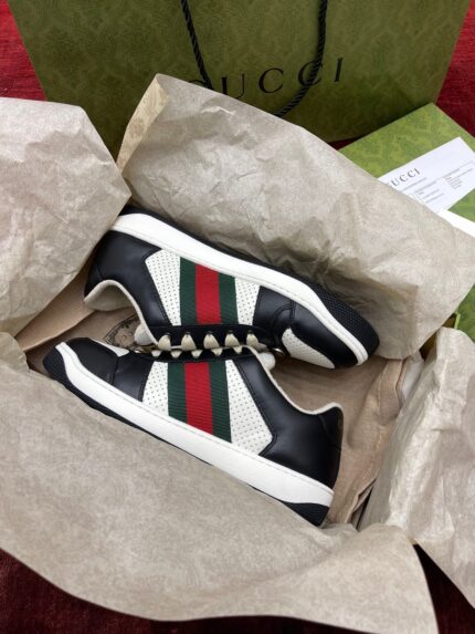 Sneakers Gucci nere con strisce rosse e verdi, packaging di lusso, stile elegante e esclusivo.