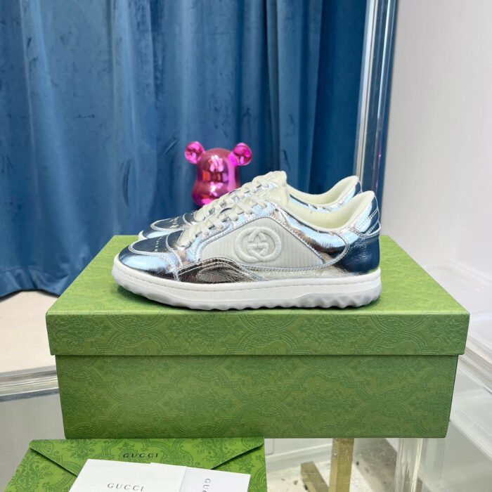 Sneakers futuristiche bianche e argento su scatola verde, sfondo blu e dettaglio rosa giocoso.
