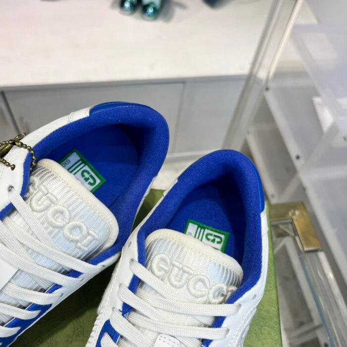 Scarpe sneakers Gucci bianche con interno blu e logo iconico in retail elegante.