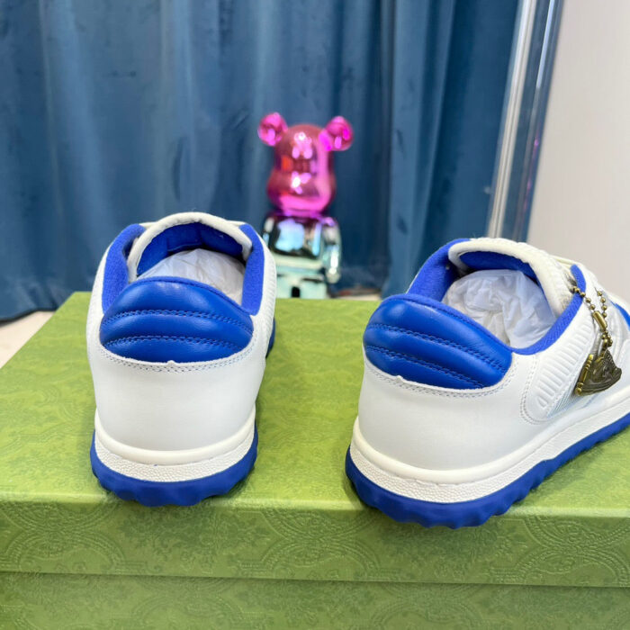 Sneakers bianche con dettagli blu, figura giocosa rosa e sfondo blu, stile streetwear giovane.