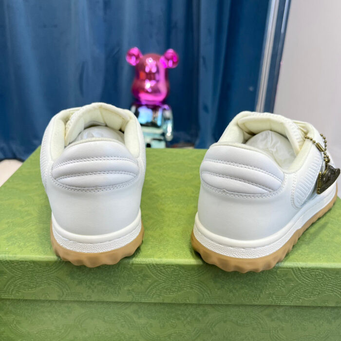 Sneakers bianche con suola gommata, sfondo colorato con figura di orsetto stilizzato.