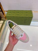 Sneaker elegante con dettagli rosa, su superficie riflessa con scatola verde di design raffinato.